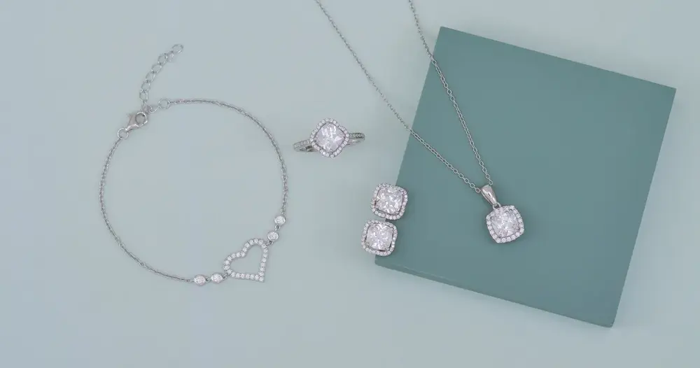 Pulseira, anel, brincos e colar de prata com pedras sobre fundo verde claro