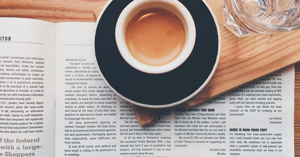 Xícara de café sobre um jornal ao lado de um copo de água
